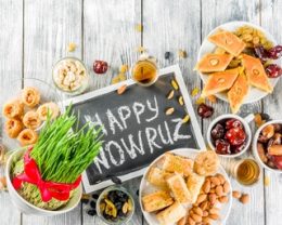 Happy Nowruz holiday background. Celebrating Nowruz sweets and treats- baklava, various dried fruits,  nuts, seeds, wooden background with green grass, copy space top view